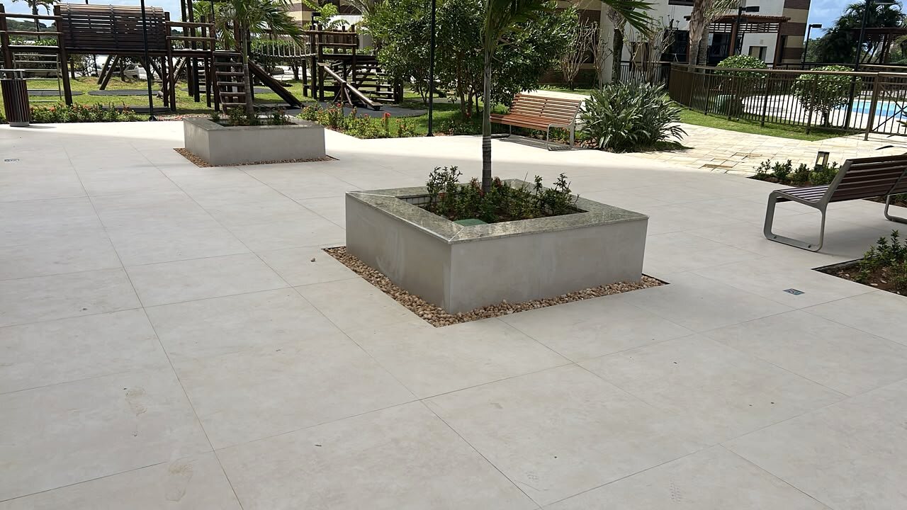 Área externa do Condomínio Lumno com piso claro, jardineiras e bancos.